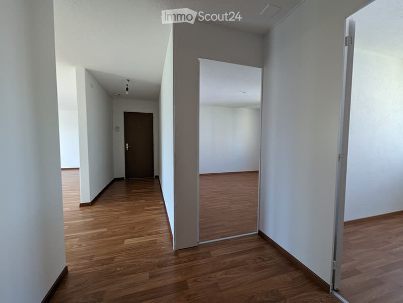 Empty hallway with wooden flooring, white walls, and a closed door at the end.