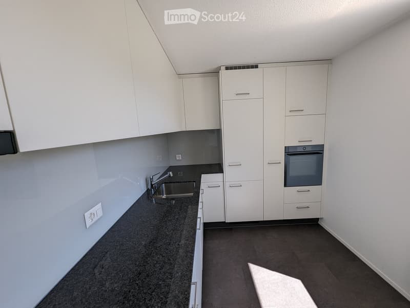 Modern kitchen with white cabinets, dark granite countertops, and stainless steel sink and oven.