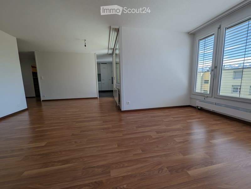 Empty room with wooden flooring, white walls, and large windows with blinds. No furniture or equipment is present.