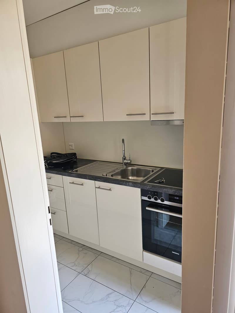 Modern kitchen with white cabinets, marble flooring, stainless steel sink, and built-in oven.