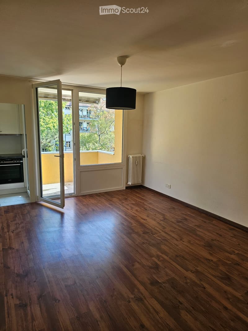 Empty room with wooden flooring, large windows, and a hanging light fixture. No furniture or equipment present.