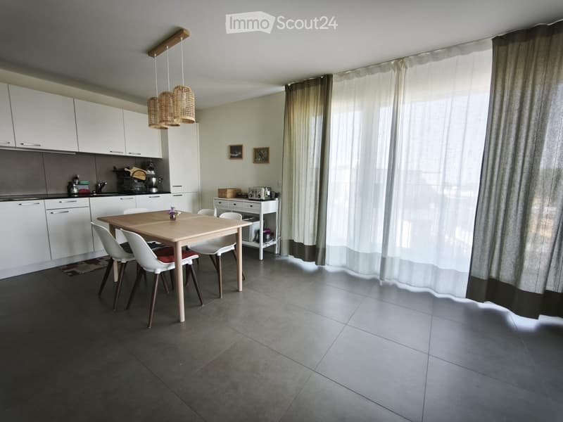 Modern kitchen and dining area with white cabinets, a wooden dining table, white chairs, and a hanging lamp.