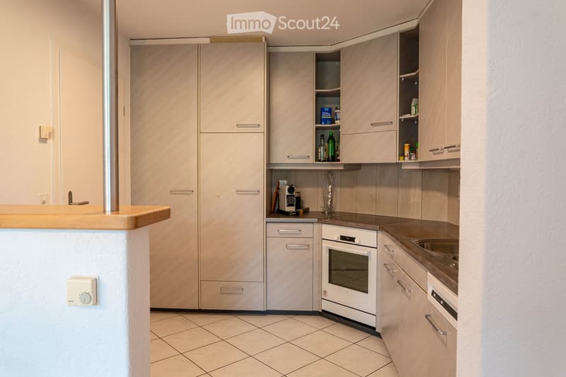 A small modern kitchen with a dishwasher and a washing machine. The kitchen has wooden countertops and white tiles.