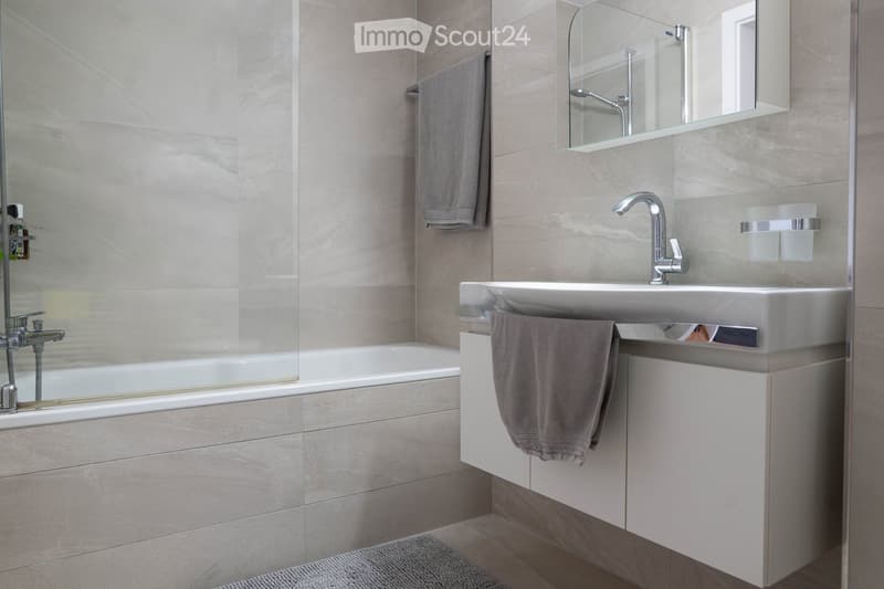 white modern bathroom with bathtub, white sink, mirror, and towel rack