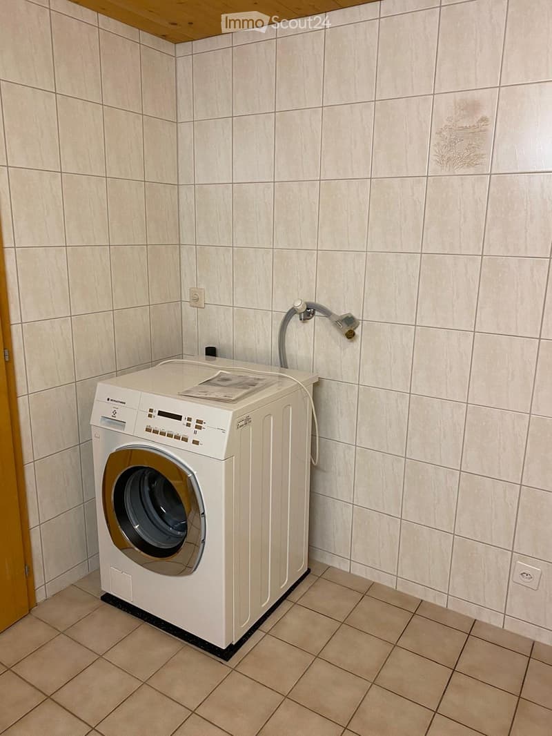 Bathroom with tiled walls and floor, featuring a white washing machine and a showerhead on the wall.