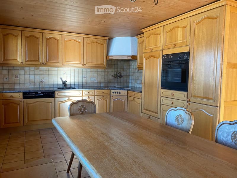 Bright kitchen with wooden cabinets, a wooden dining table with chairs, and modern appliances including an oven and dishwasher.