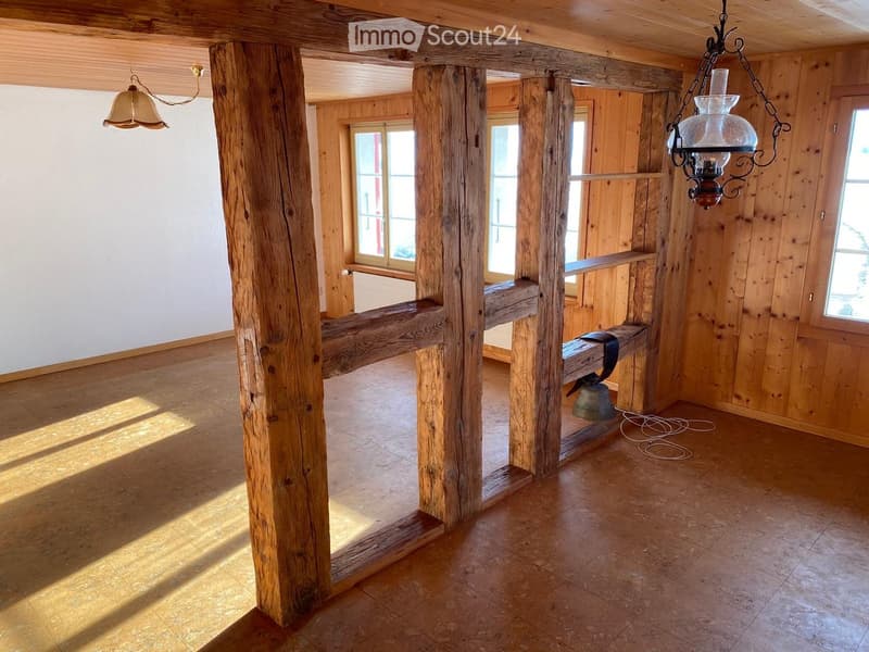 Empty room with wooden beams, wooden floor, large windows, and hanging lanterns.
