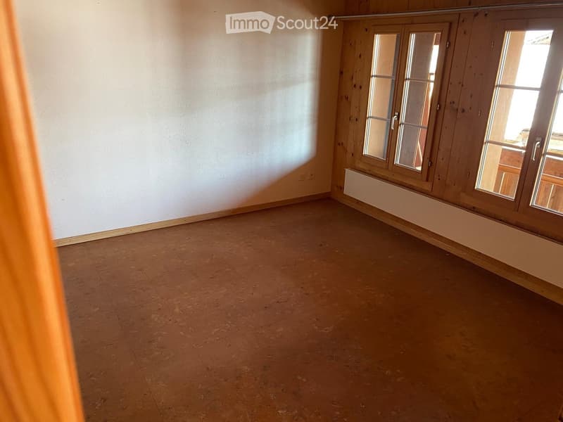 Empty room with wooden flooring, white walls, and large windows with wooden frames. No furniture or equipment present.