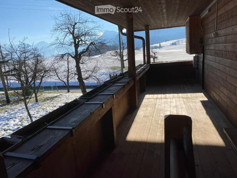 Wooden balcony with a railing, overlooking a snowy landscape and mountains.