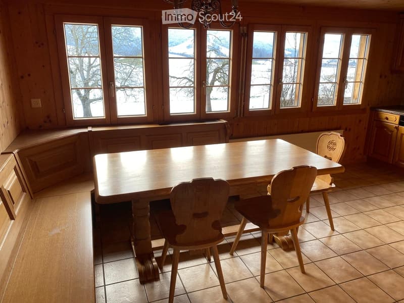 Bright kitchen with wooden walls, large windows, tiled floor, and a wooden dining table with chairs.