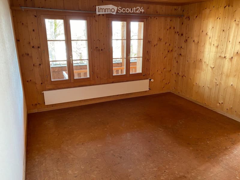 Empty room with wooden walls, tiled floor, large windows, and radiator.