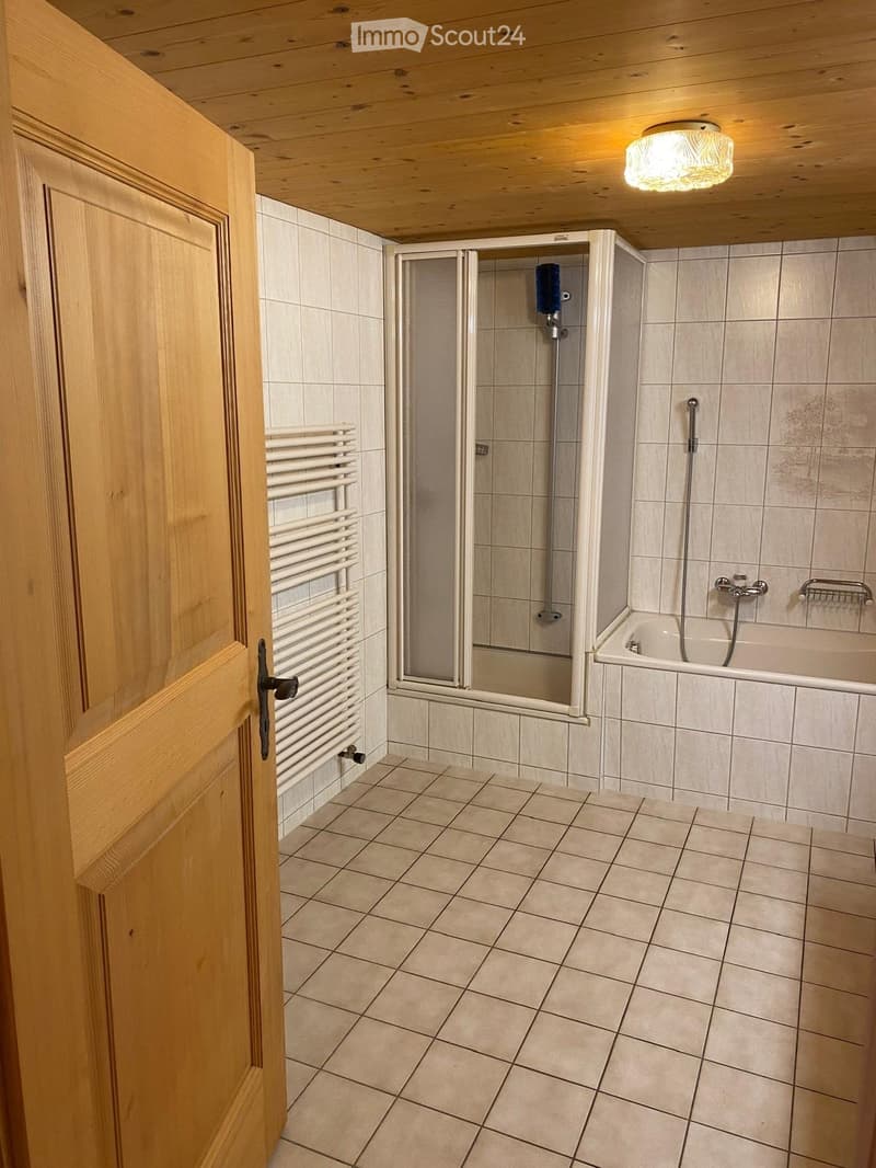 Bathroom with tiled walls and floor, featuring a bathtub, shower, and radiator. Wooden door and ceiling visible.