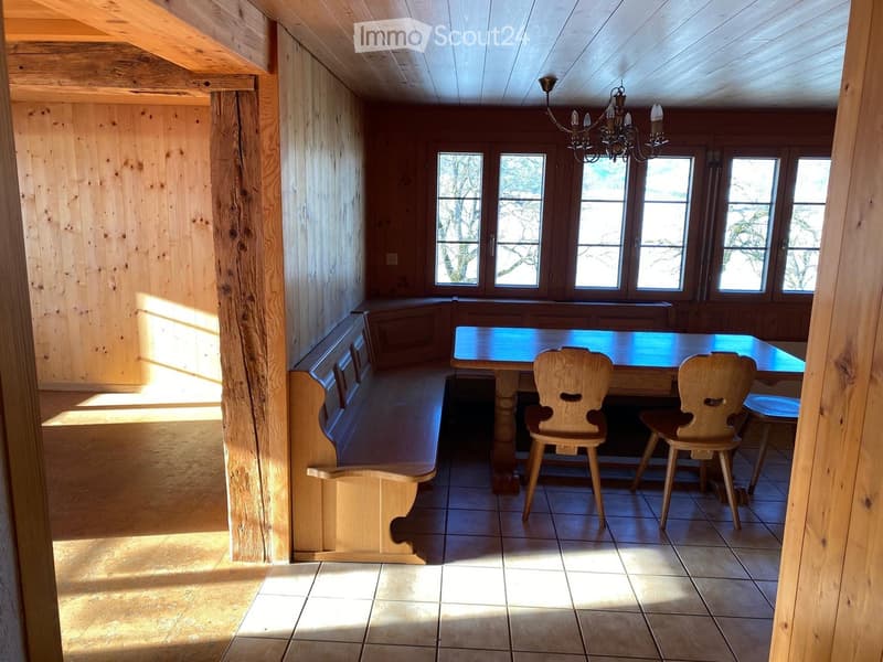 Bright, wooden-paneled kitchen with a long wooden table, two chairs, and a built-in bench along one wall. Natural light streams in through multiple windows.