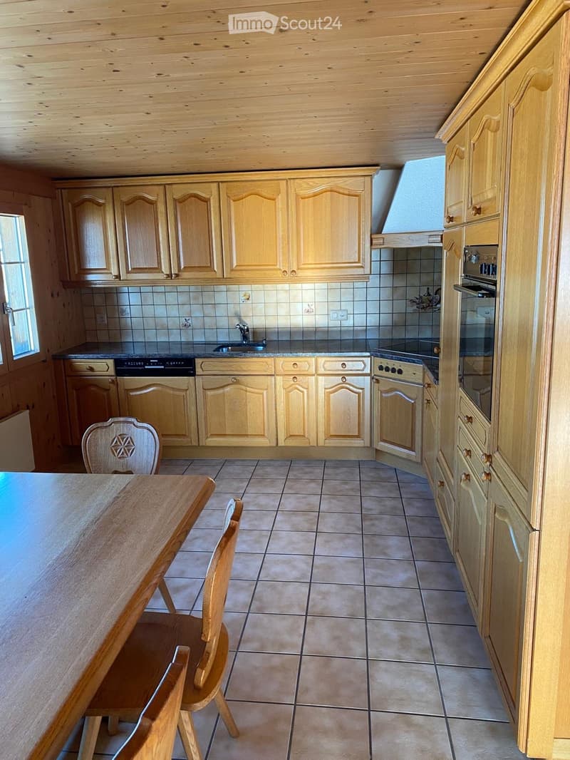 Bright kitchen with wooden cabinets, tiled backsplash, and a central island. Includes a wooden dining table and chairs.