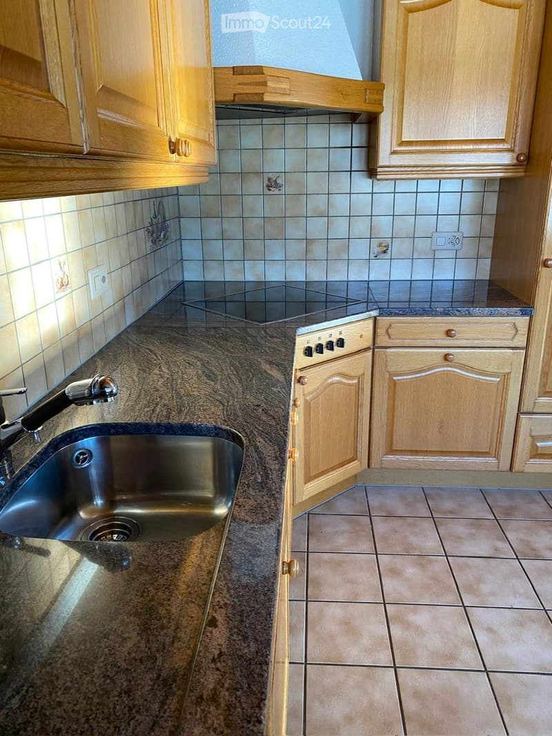 A modern kitchen with light wooden cabinets, a stainless steel sink, and a granite countertop.