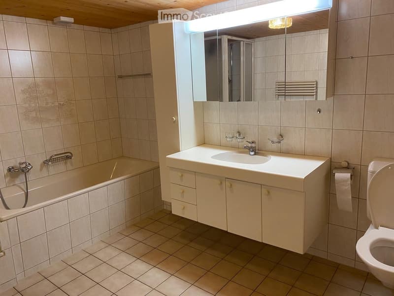 Bathroom with beige tiled walls and floor, featuring a bathtub, sink with faucet, mirror, cabinet, toilet, and a radiator.