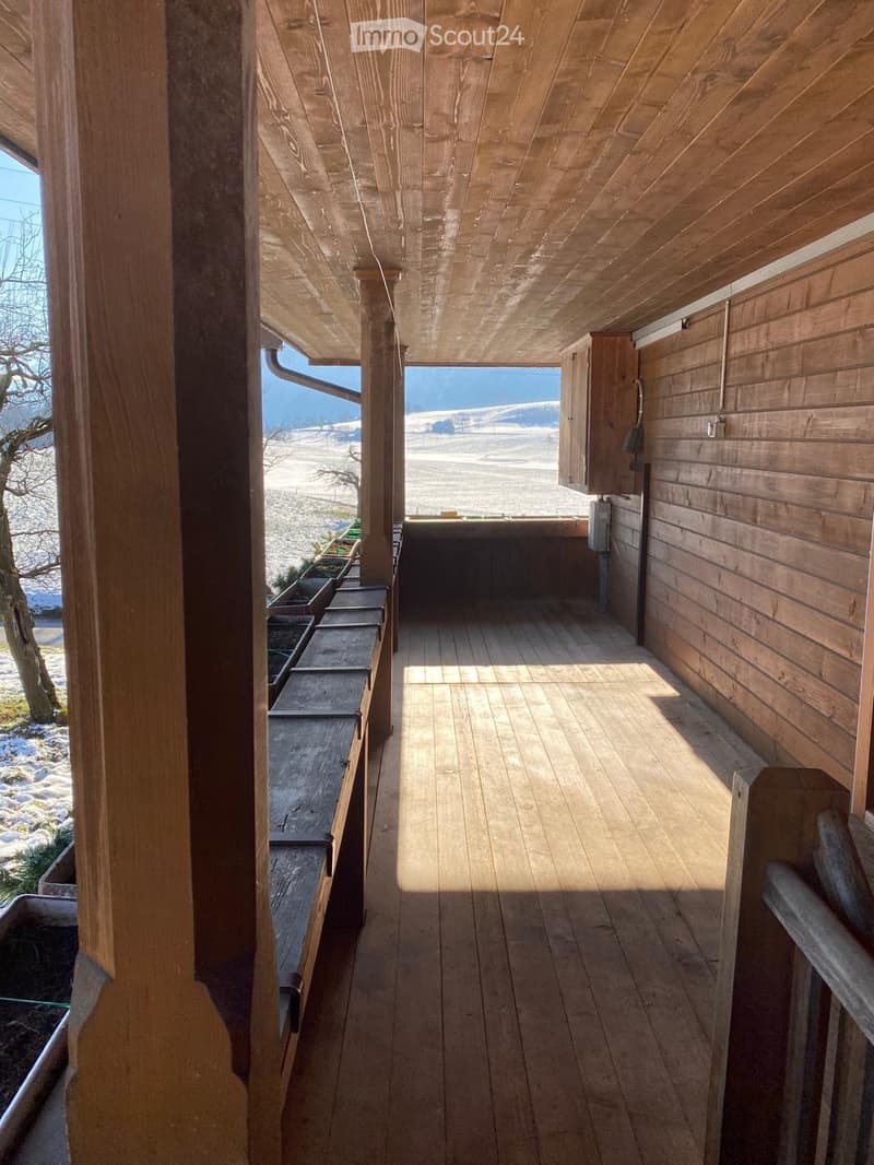 Wooden balcony with a view of a snowy landscape, featuring wooden railings and a small table.