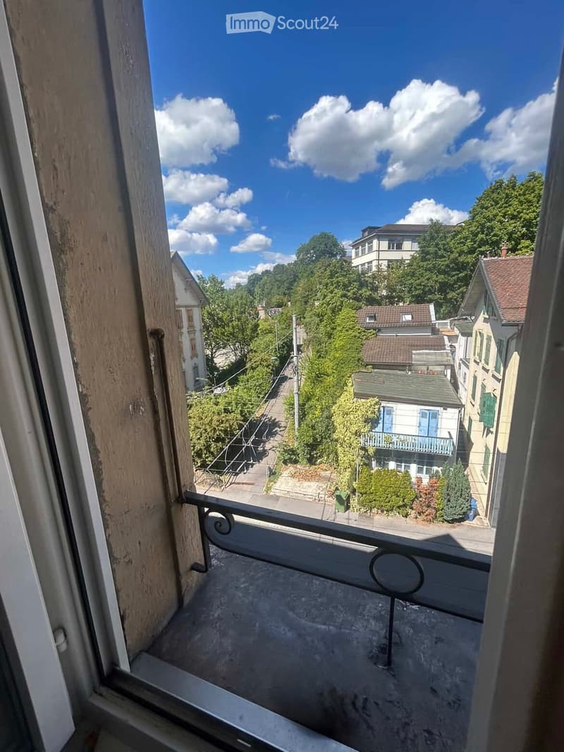 Balcony overlooking a residential street with houses, trees, and a clear blue sky.