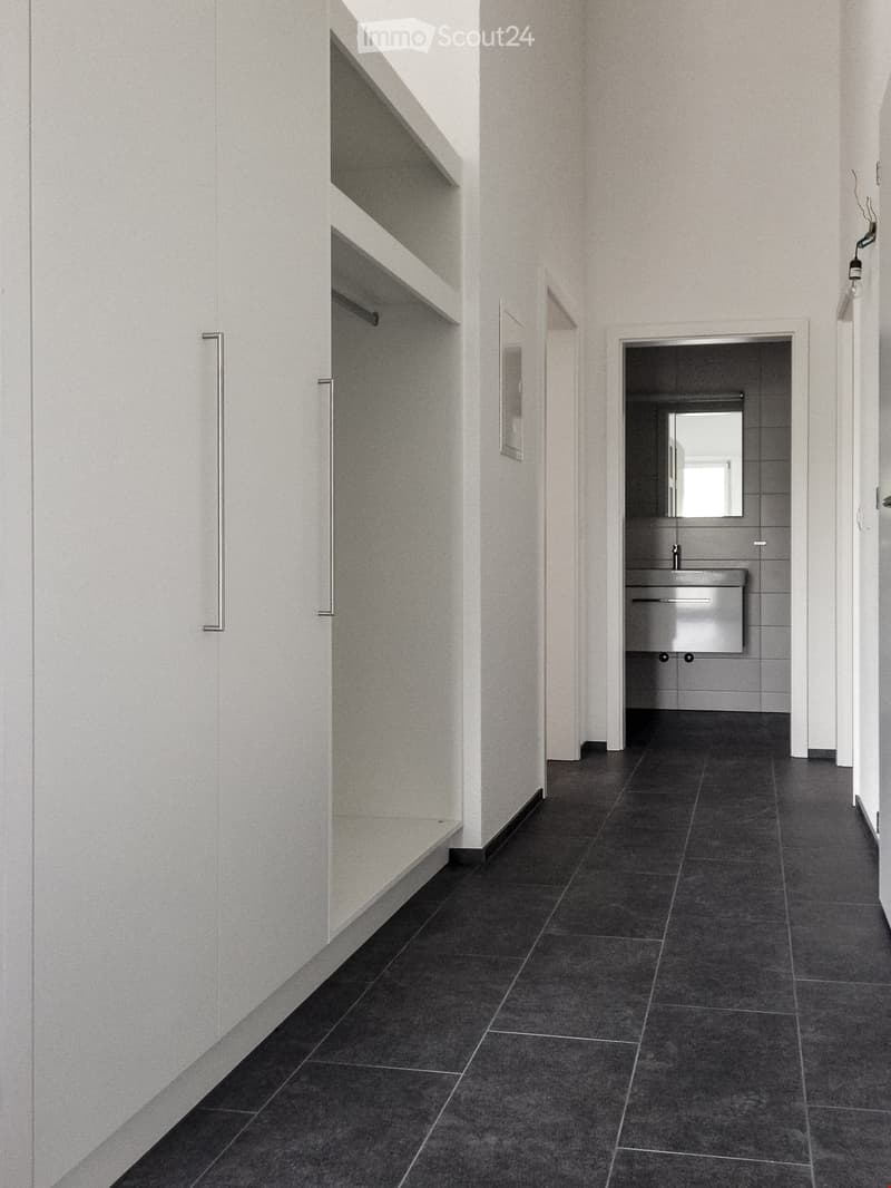 Modern hallway with dark tiled flooring, white walls, built-in shelving unit, and a small adjacent bathroom with a sink and mirror.
