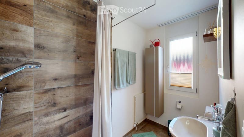 Modern bathroom with wooden wall paneling, a shower area with a glass curtain, a sink with a faucet, a towel rack, and a window with blinds.