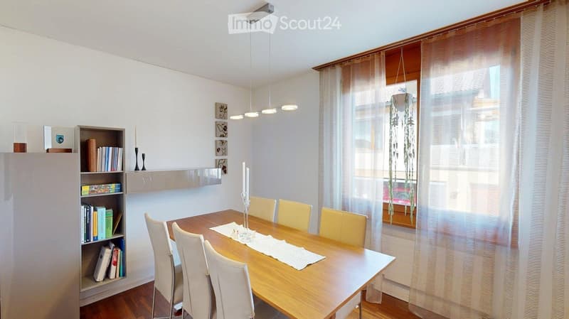 Dining room with a wooden dining table, six chairs, a bookshelf, and a hanging light fixture.
