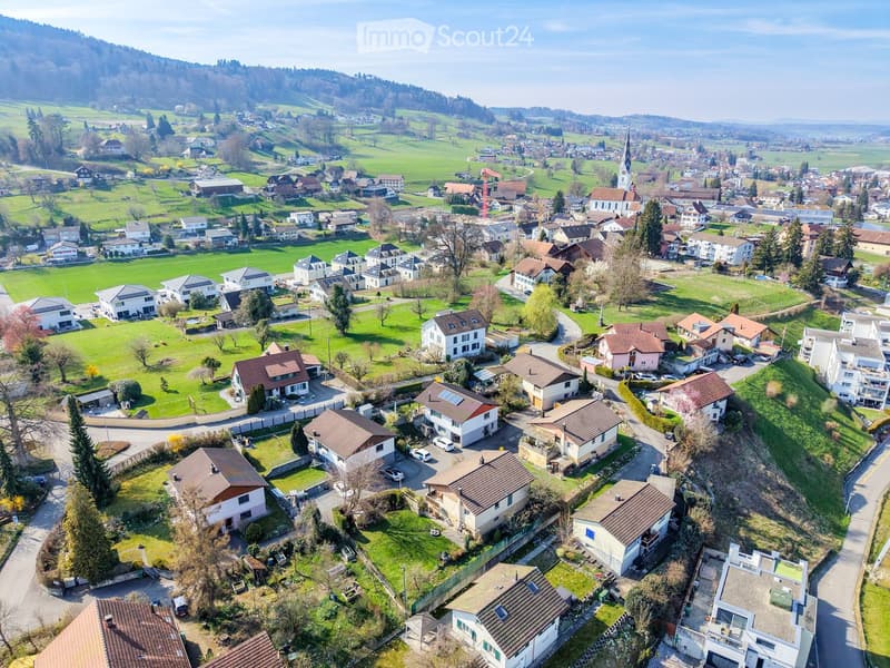 Aerial view of a suburban neighborhood with numerous houses, green lawns, and surrounding hills.
