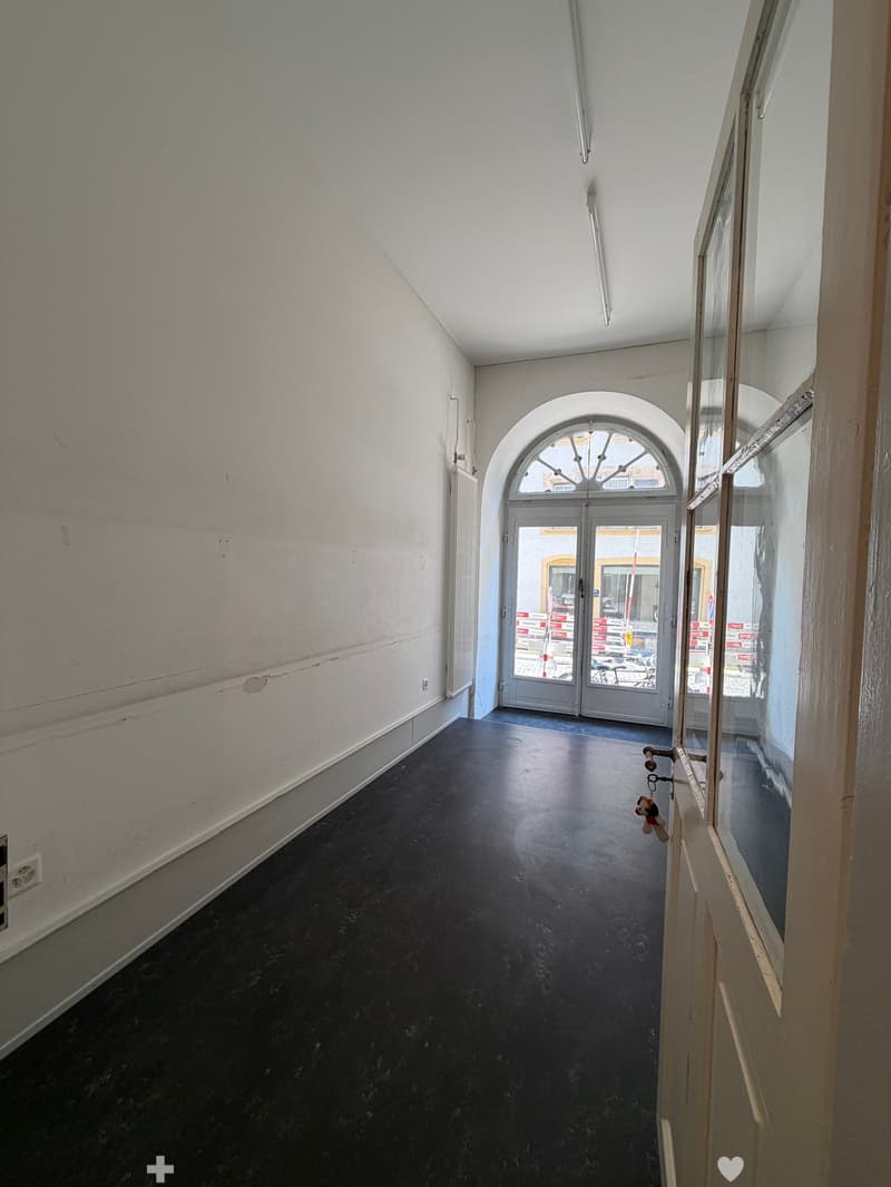 Empty hallway with dark flooring, white walls, and an arched doorway leading outside.