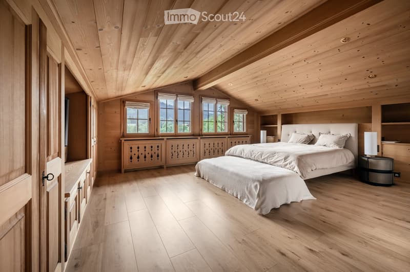 Spacious bedroom with wooden walls, ceiling, and flooring, large windows with views, a large bed with bench, nightstand, and built-in cabinets and shelves.