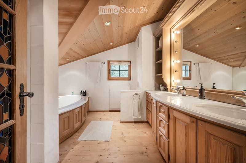 Cozy bathroom with wooden ceiling and flooring, featuring a bathtub, double sink, large mirror, and wooden cabinets.