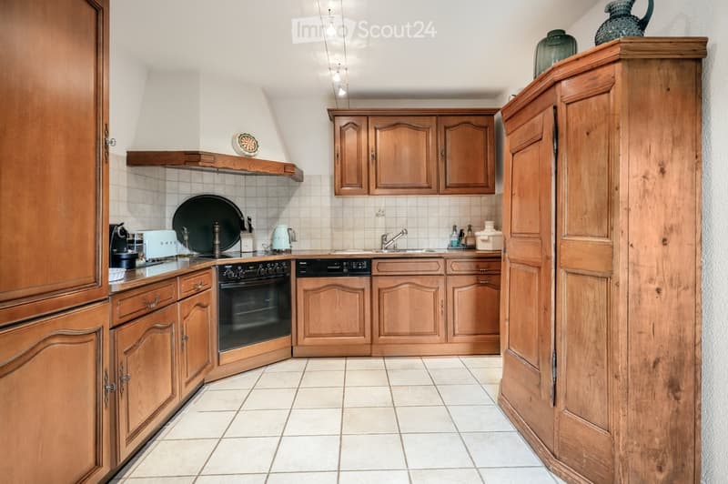 Bright kitchen with wooden cabinets, tiled floor, and modern appliances including an oven and dishwasher. Countertop features a coffee maker, a plate, and a vase.