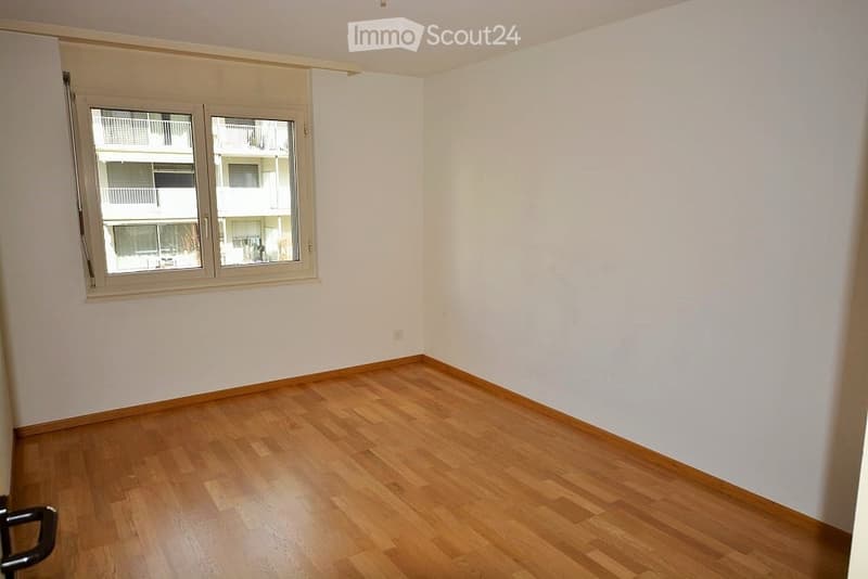 Empty room with wooden flooring and white walls, featuring a window with a view of a building exterior.