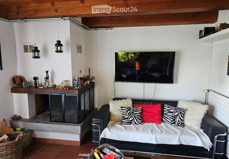 Living room with a black leather sofa, colorful throw pillows, a coffee table, a mounted TV, and a fireplace with decorative items on the mantel.