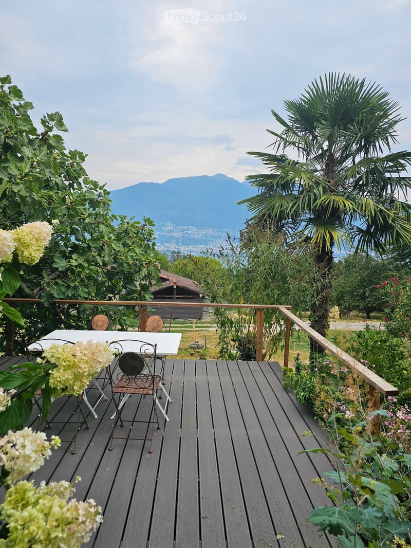 Wooden deck with a table and chairs, surrounded by lush greenery and offering a scenic mountain view.