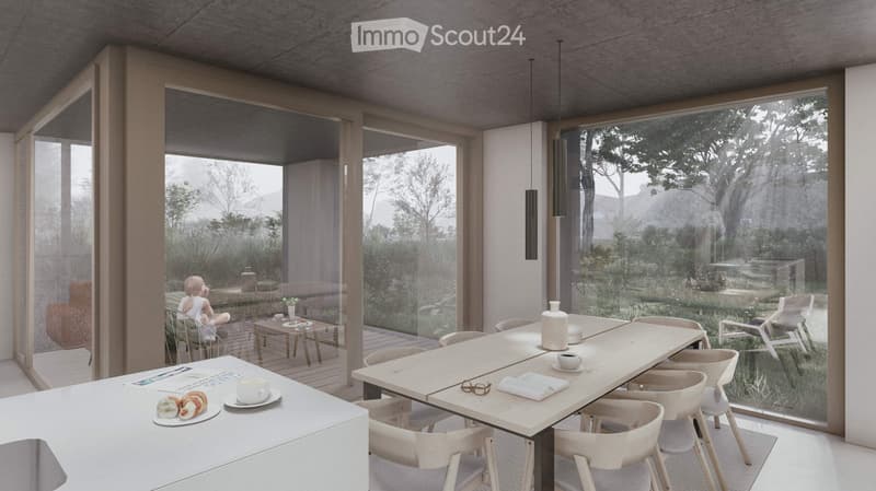 Spacious open-plan living and dining area with large windows offering a scenic view of the surrounding nature. The room features a dining table with chairs, a kitchen counter, and a cozy seating area with a doll figurine. The overall design is minimalist
