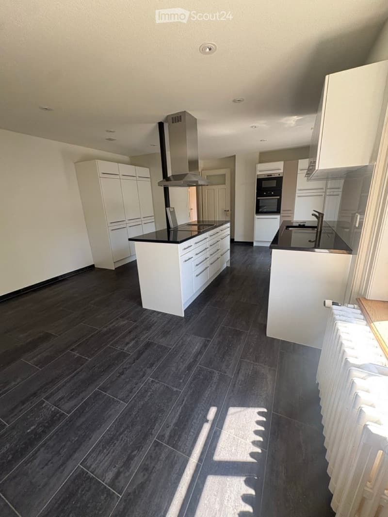 Modern kitchen with white cabinets, black countertops, dark tiled floor, and stainless steel appliances including a range hood and oven.