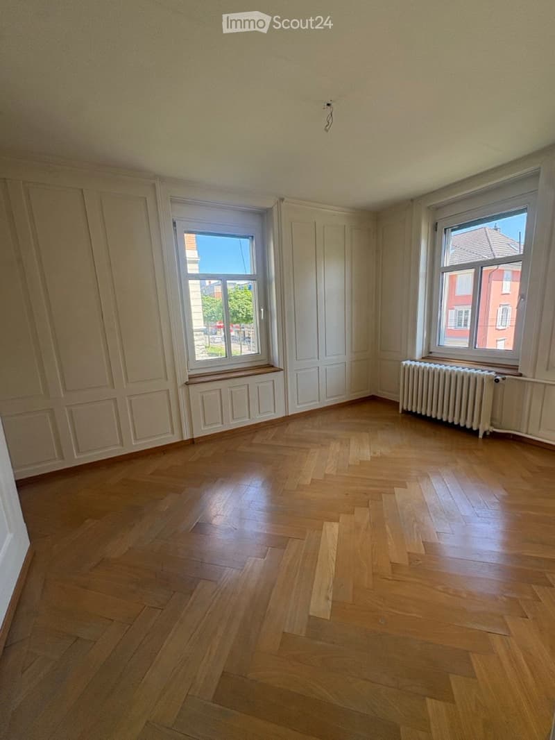 Empty room with wooden flooring, white walls, and two windows with radiators beneath them.