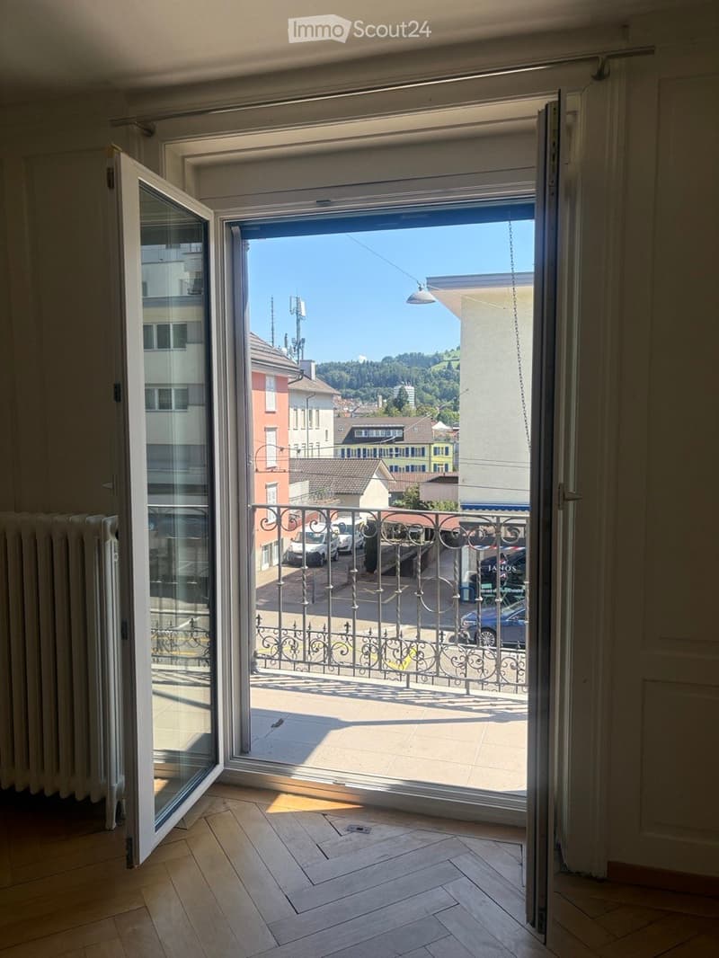 Open balcony with metal railing, wooden floor, and cityscape view.