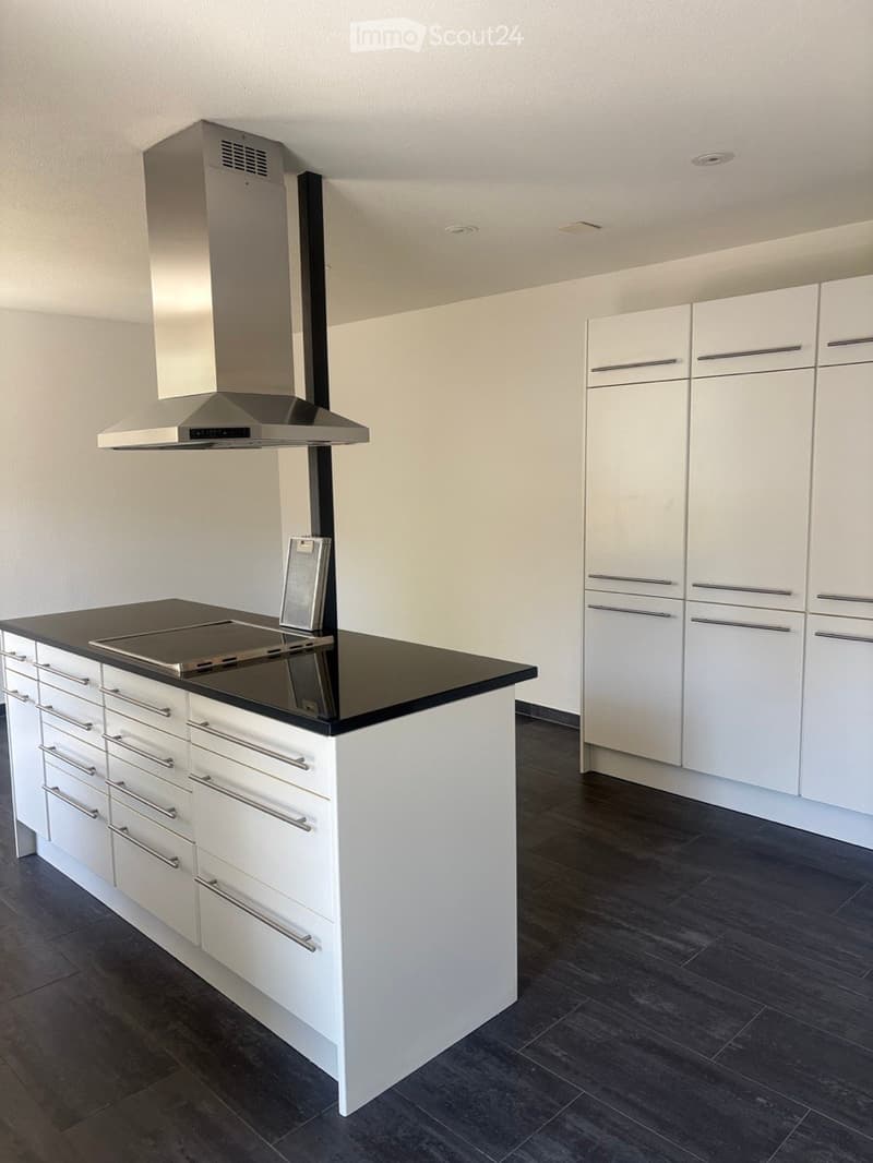 Modern kitchen with white cabinets, a black countertop island, and a stainless steel range hood.