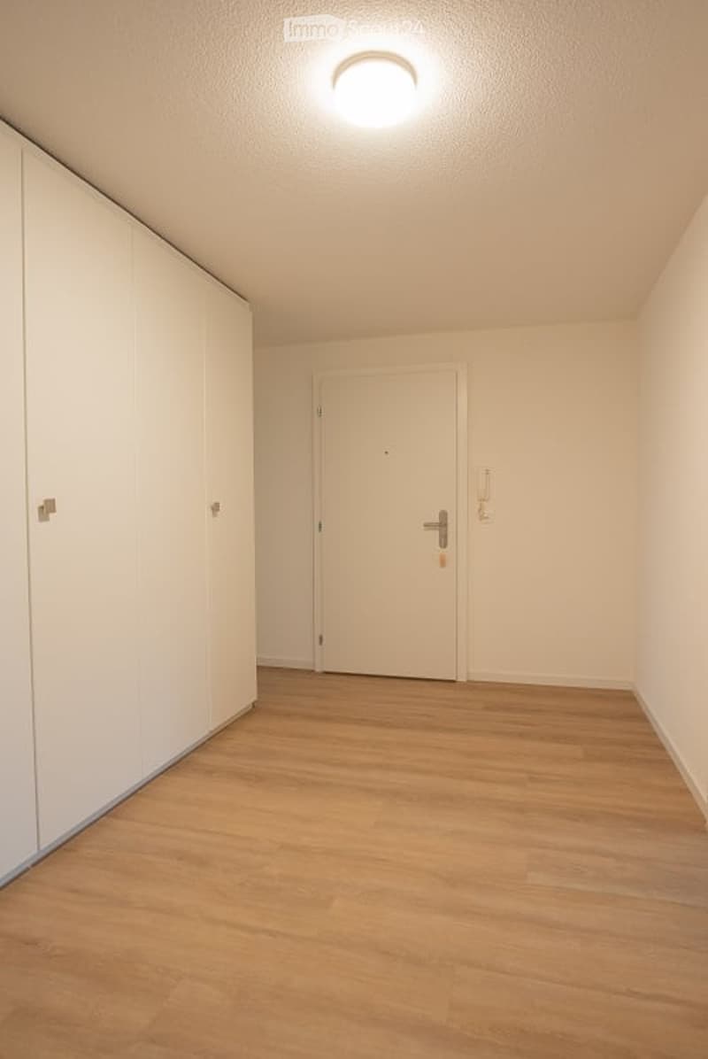 Empty hallway with wooden flooring, white walls, and a closed door at the end.