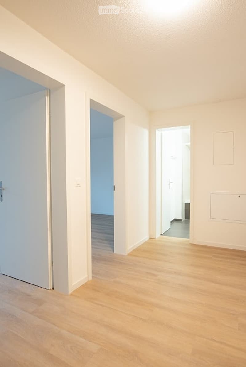 Empty hallway with light wooden flooring, white walls, and multiple doors leading to other rooms.
