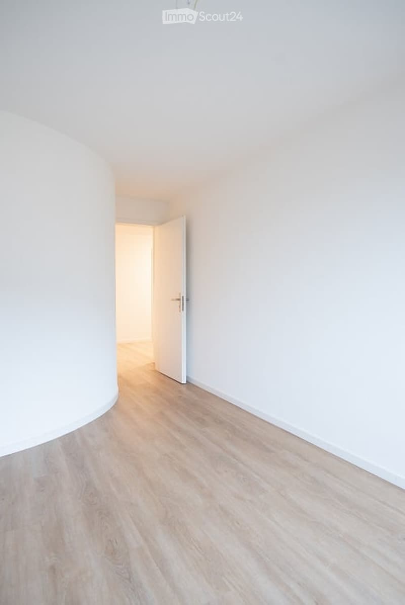 Empty room with light wooden flooring and white walls, featuring an open doorway leading to another space.
