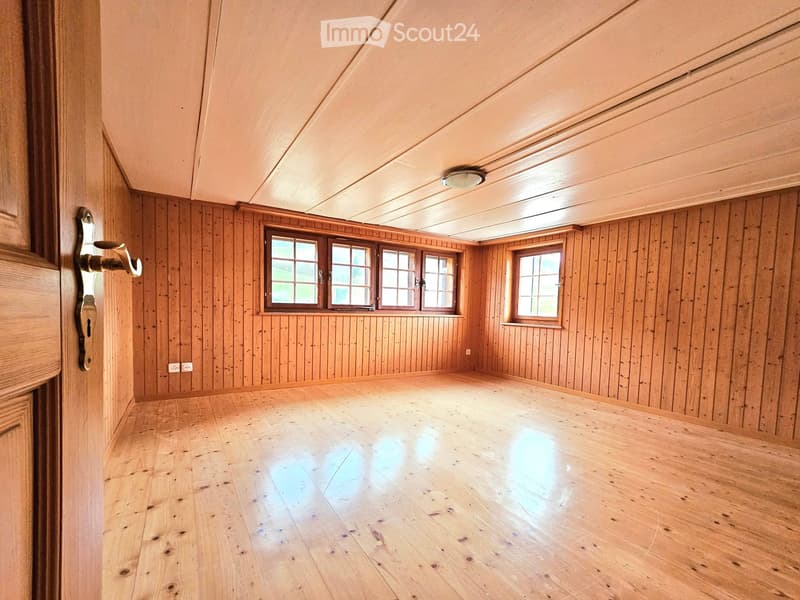 Empty room with wooden walls and floor, large windows, and a door.