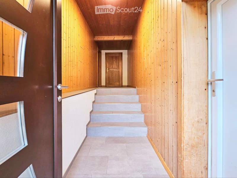 A narrow hallway with wooden panel walls, a staircase leading upwards, and a door at the end.
