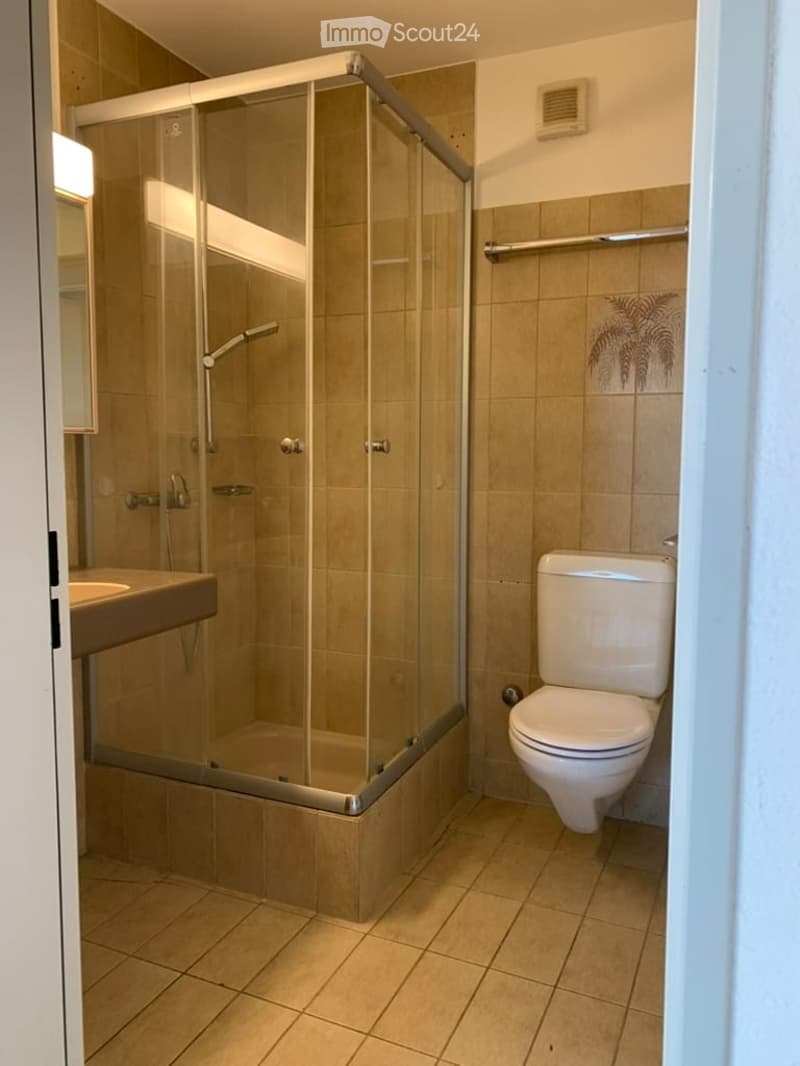 Modern bathroom with beige tiles, glass-enclosed shower, toilet, sink, and mirror.
