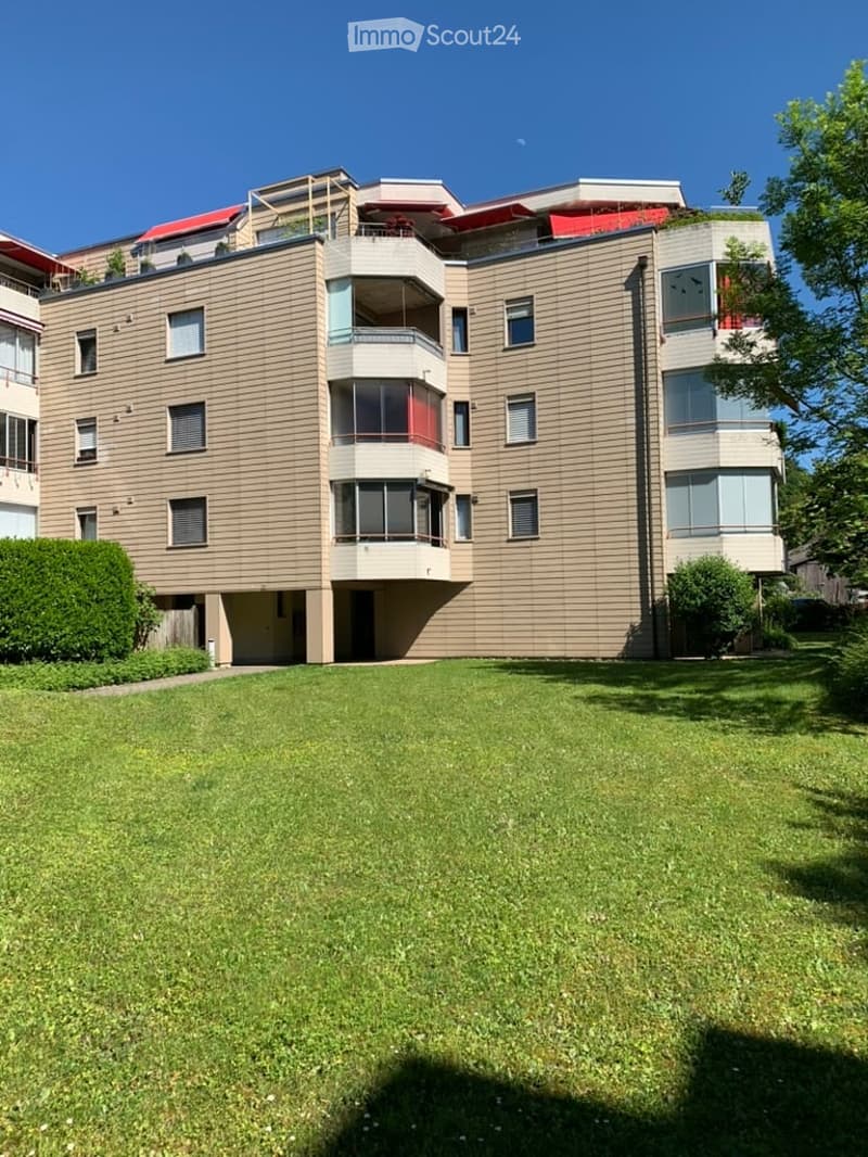 Modern multi-story building with balconies, large windows, and a well-maintained lawn in front.
