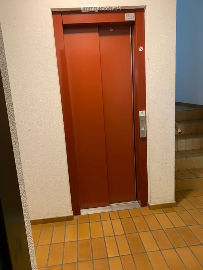Hallway with a red elevator door, tiled floor, and a staircase visible to the right.