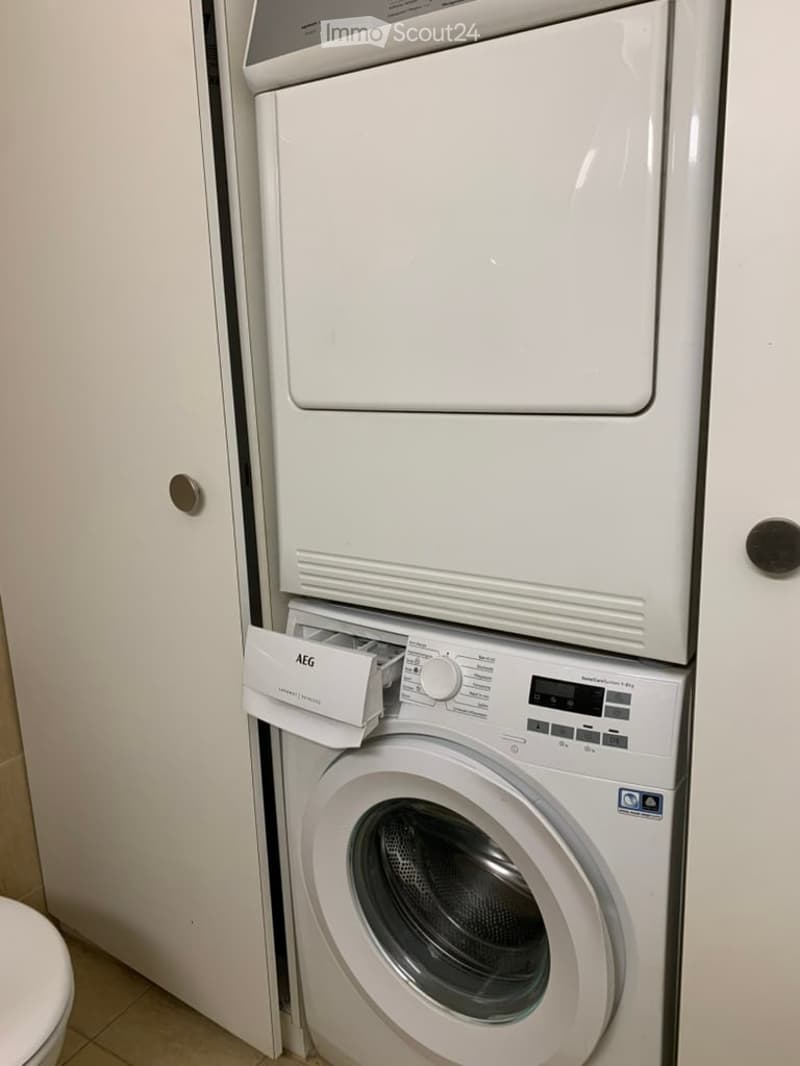 Bathroom with a white washing machine and dryer stacked vertically, control panel visible, white tiled floor.