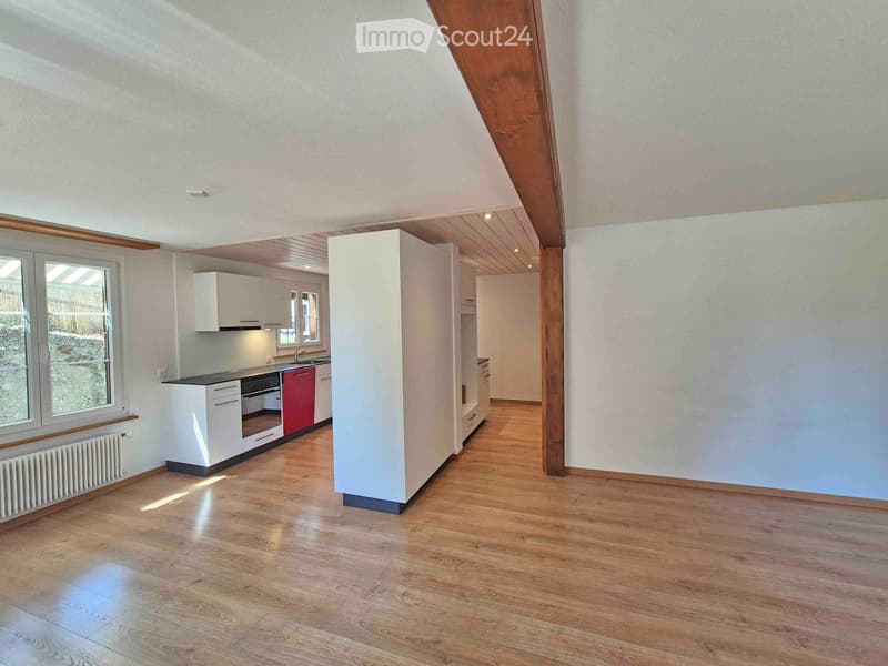 Open-plan living and kitchen area with wooden flooring, white kitchen cabinets, red oven, and large windows.