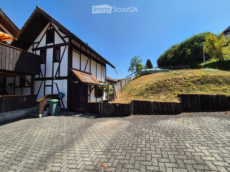 Traditional half-timbered house with white and black exterior, wooden balcony, and cobblestone driveway.