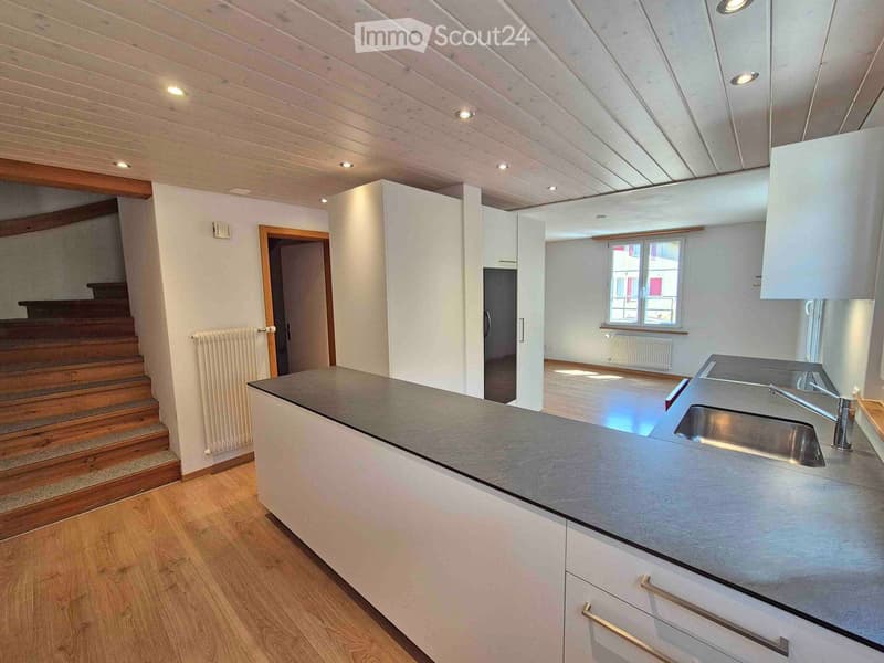 Modern kitchen with white cabinets, stainless steel sink, and a wooden staircase leading to another level.